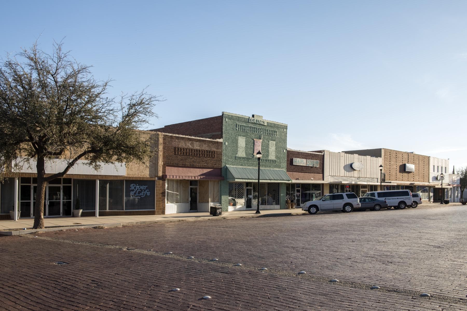 Brick paving and a row of historic commercial storefronts in downtown Lamesa under a clear sky.